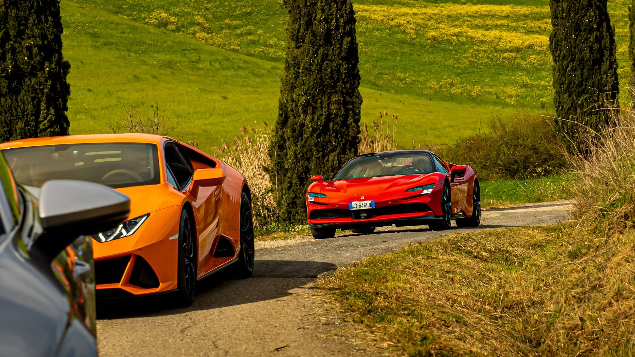 Supercars on a country road between cypresses and green hills